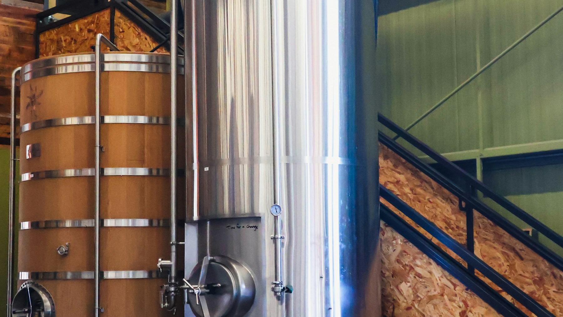 Fermentation tanks inside Anchorage Brewing Company, including a reflective stainless steel tank beside wood-clad vessels