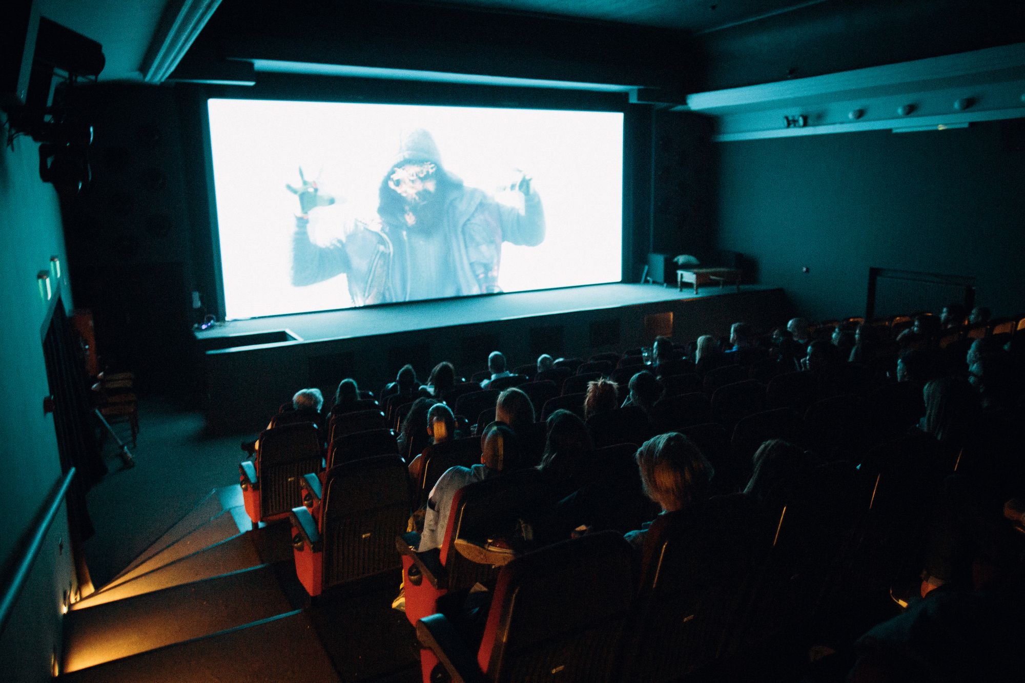 Moviegoers sit in a dark cinema facing a brightly lit screen