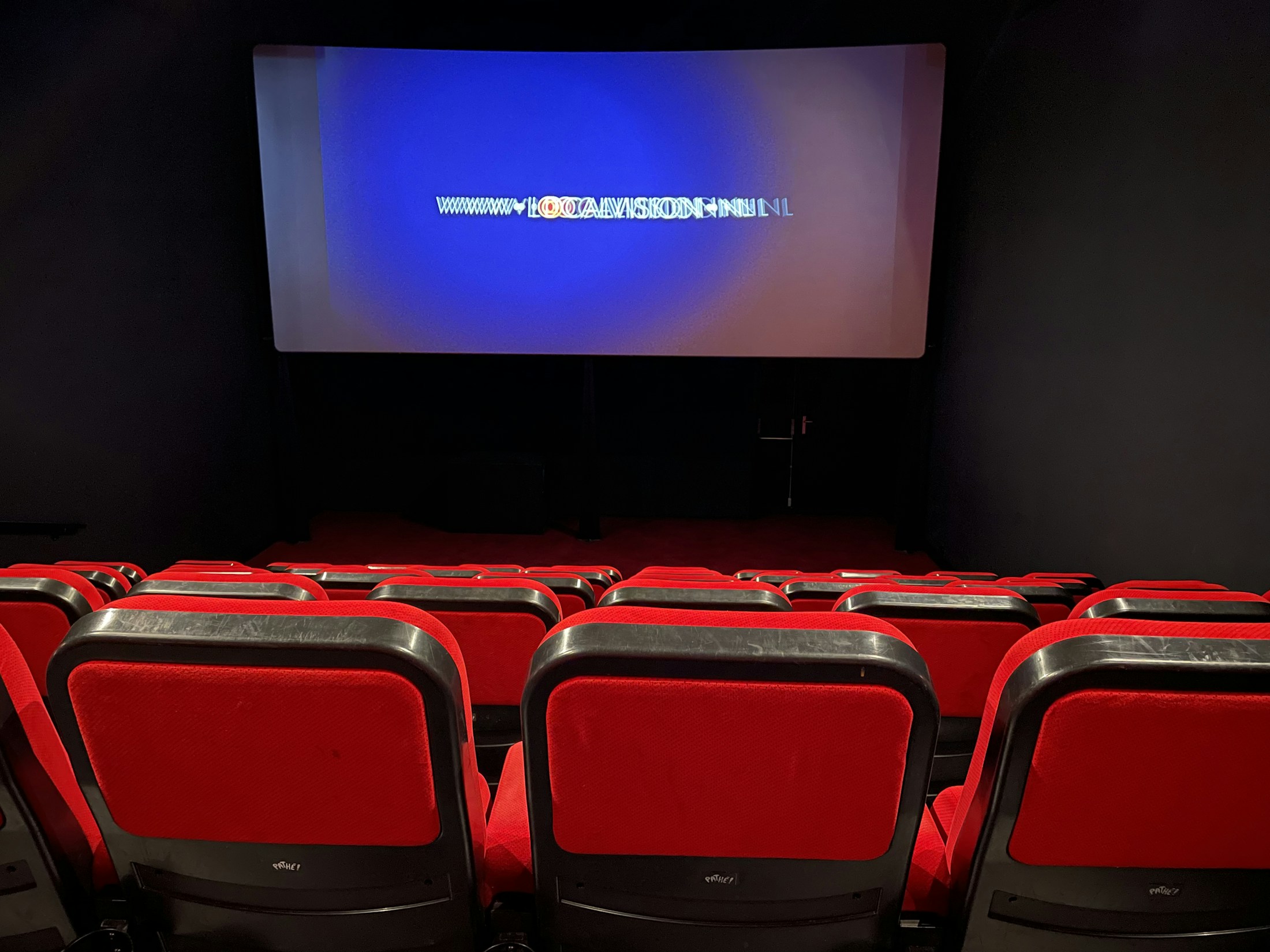 Rows of red seats face a screen inside a small movie theater