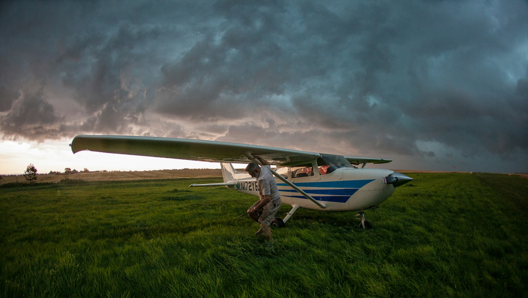 A small airplane sits in a green field beneath dark storm clouds