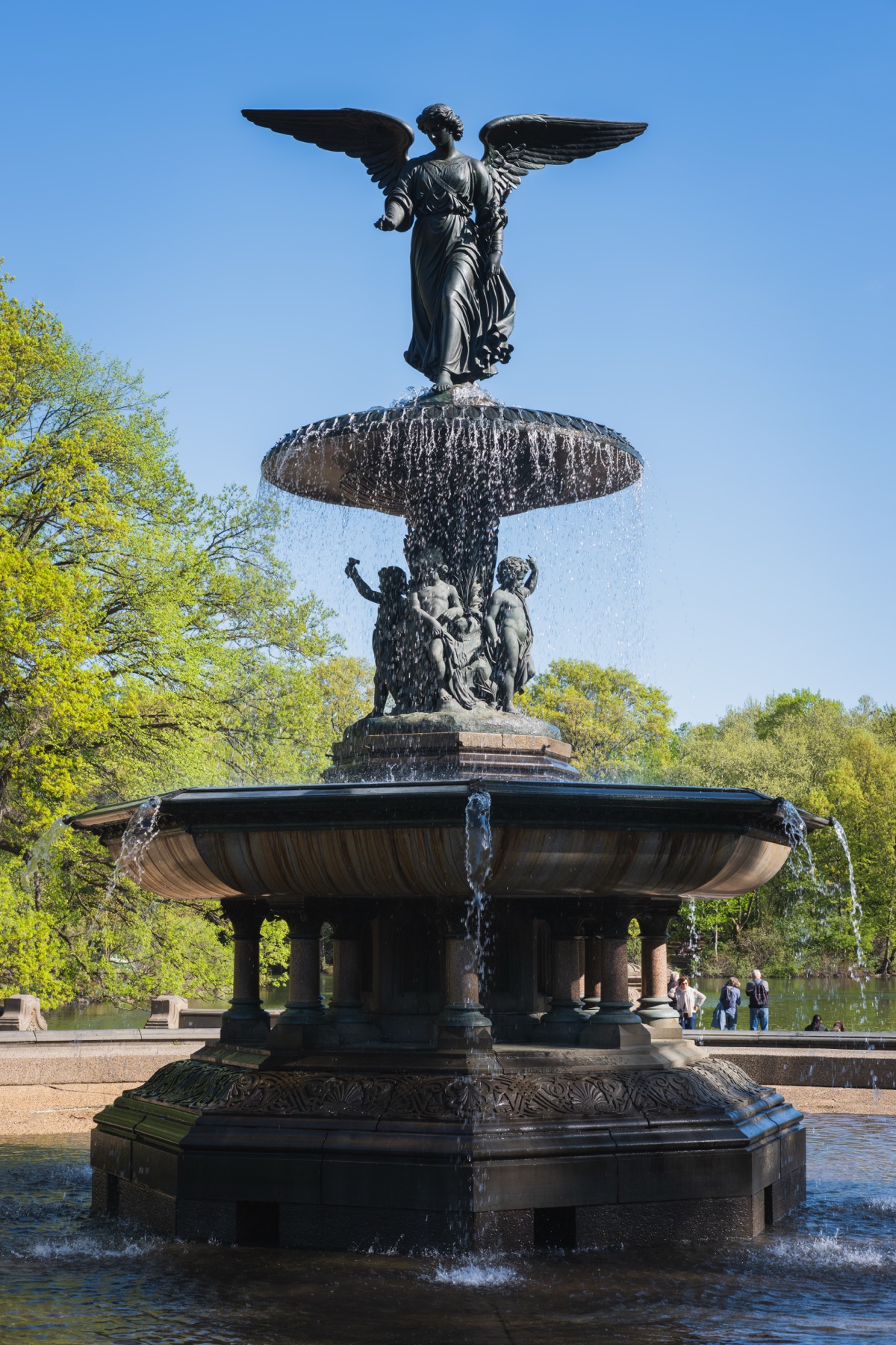 Close view of Emma Stebbins’s bronze Angel of the Waters above the upper fountain basin, with the lily in her left hand and the four smaller figures visible below.
