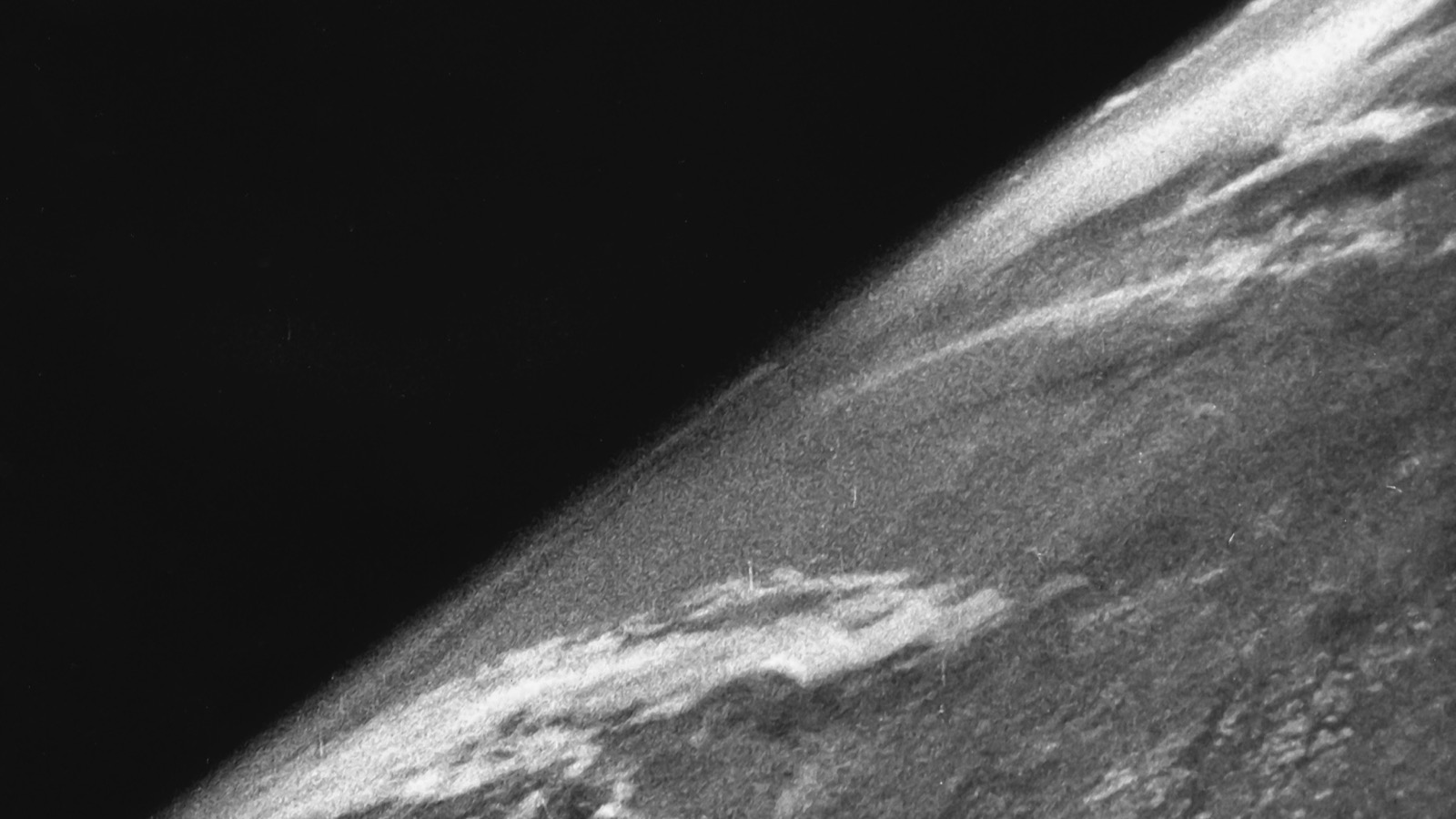 Grainy black-and-white 1946 photograph showing Earth’s curved horizon and clouds beneath black space.