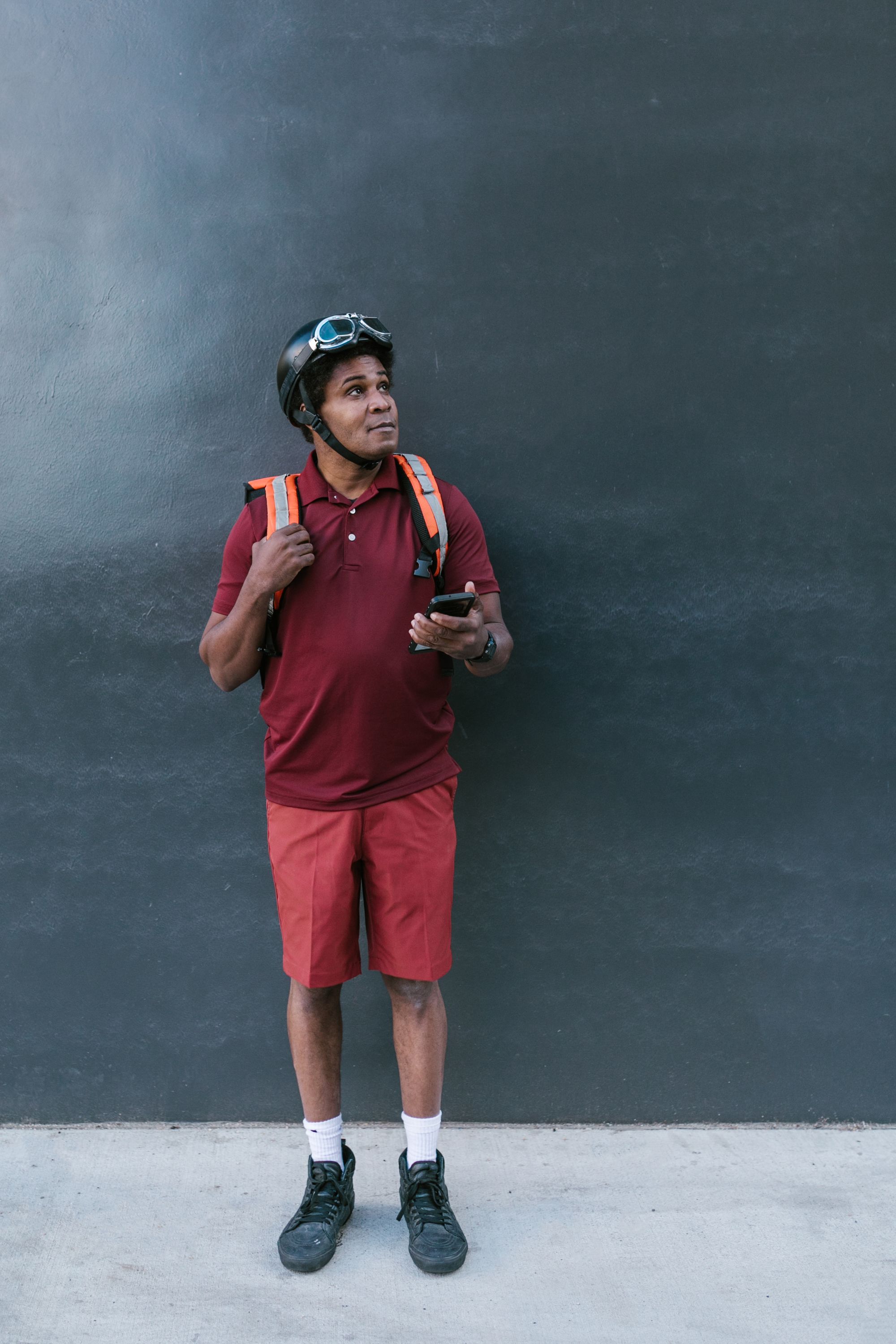 A delivery worker wearing a helmet holds a phone beside a dark wall
