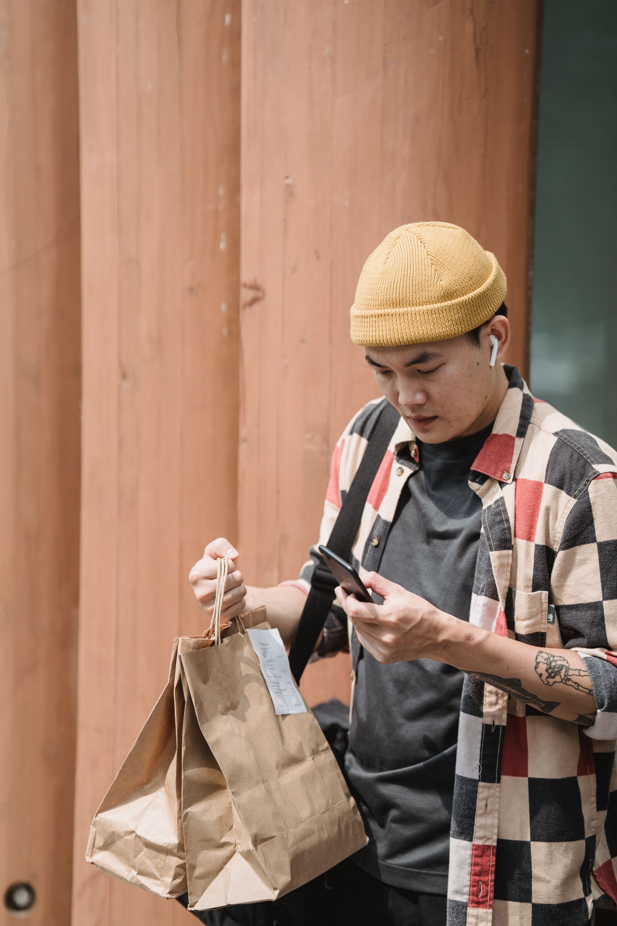 A food courier checks a phone while holding two brown paper takeout bags
