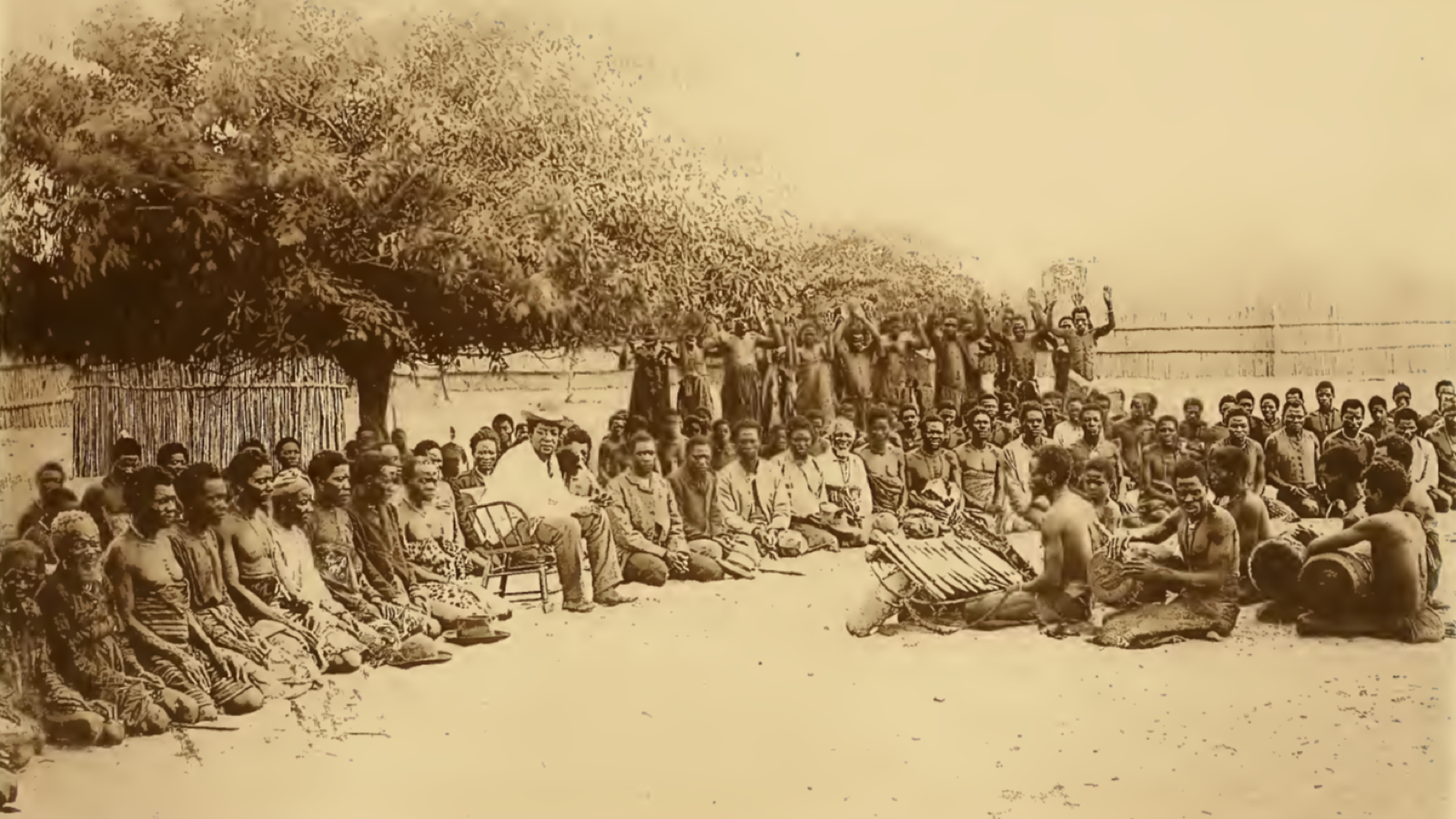 Sepia historical image of a large outdoor gathering in Barotseland, with seated people forming a wide circle beneath a tree.