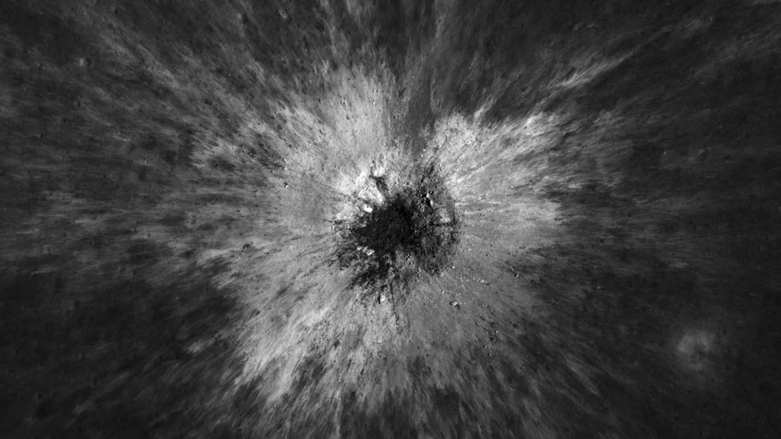 A dark circular crater surrounded by bright rays of ejected material on the gray lunar surface