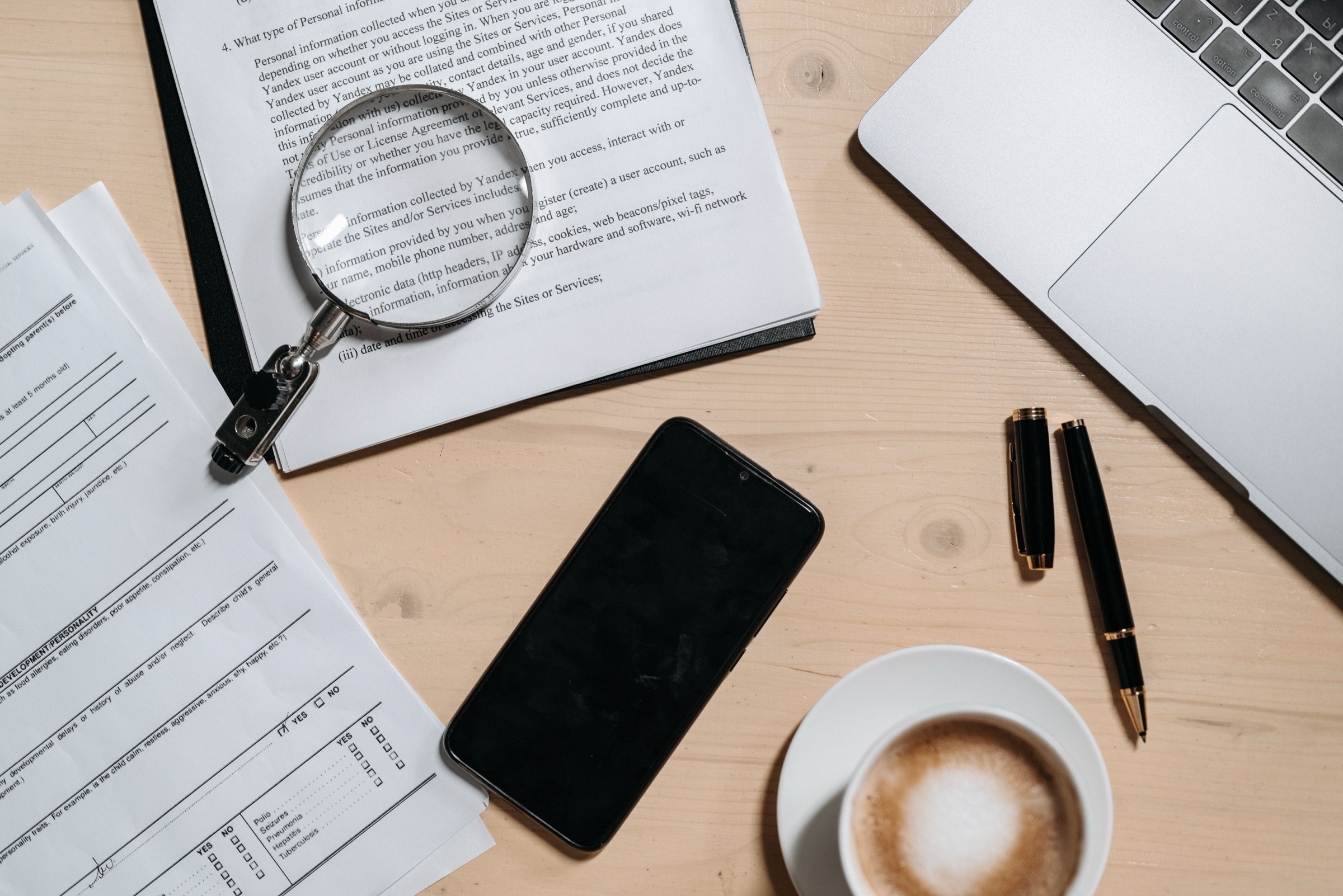 Documents, a laptop, a phone, and a magnifying glass arranged on a working desk