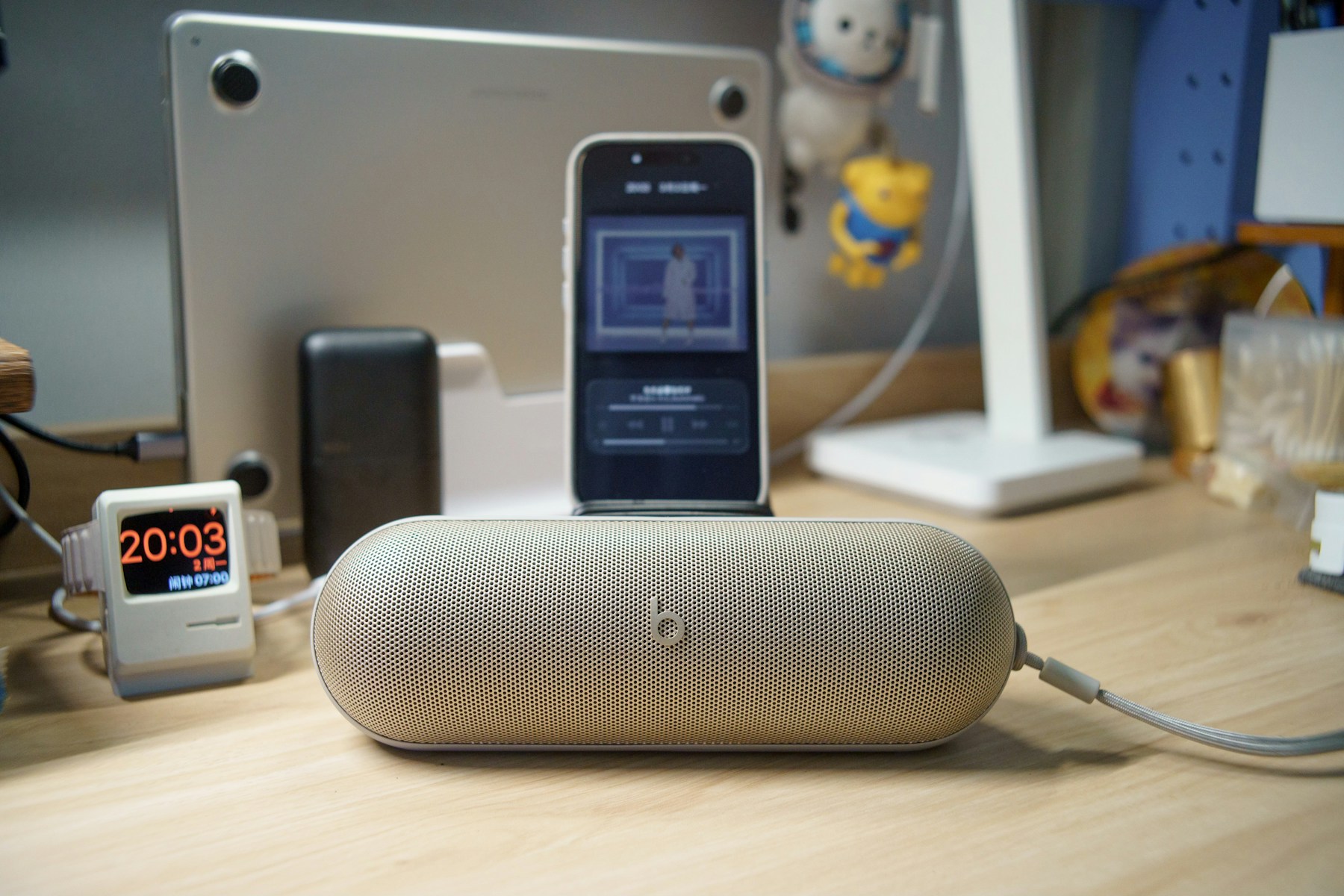 A smartphone rests behind a portable speaker on a desk